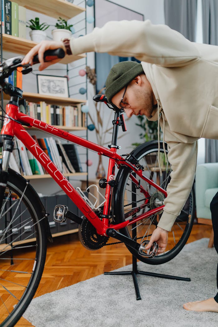Adult male in casual wear tuning a red bicycle indoors.