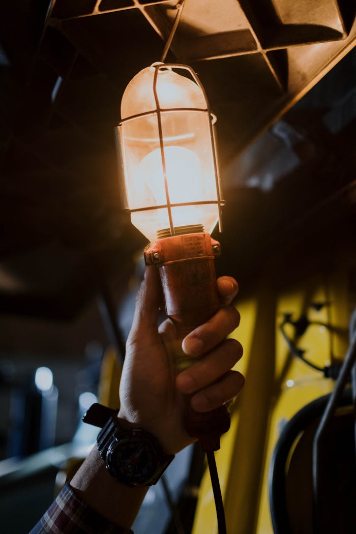 A hand holds a vintage garage work light, illuminating a dark space.